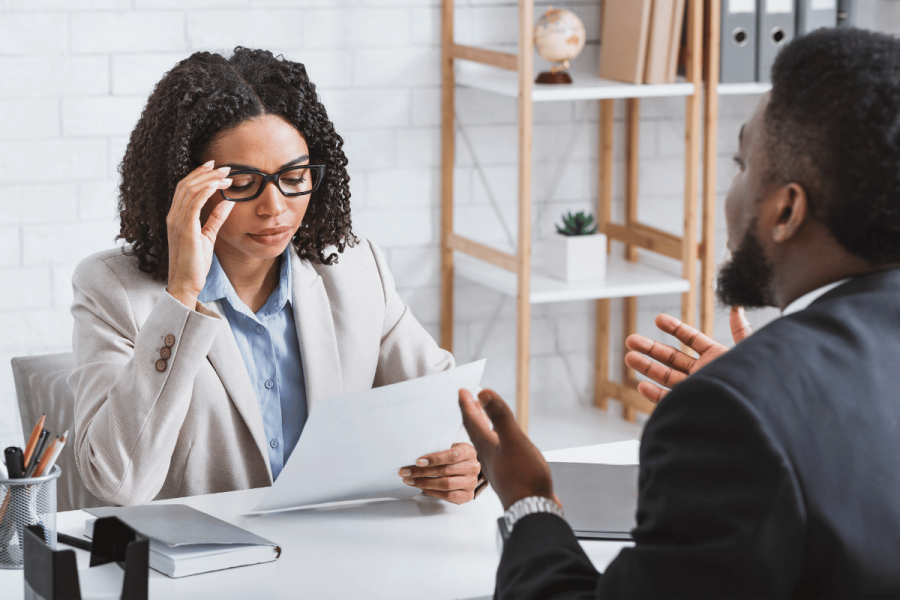 Woman wearing glasses holds a piece of paper while interviewing a job candidate.