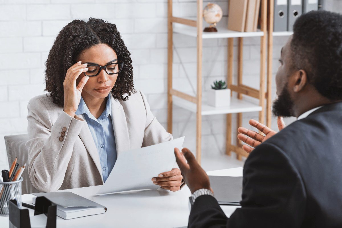 Woman wearing glasses holds a piece of paper while interviewing a job candidate.