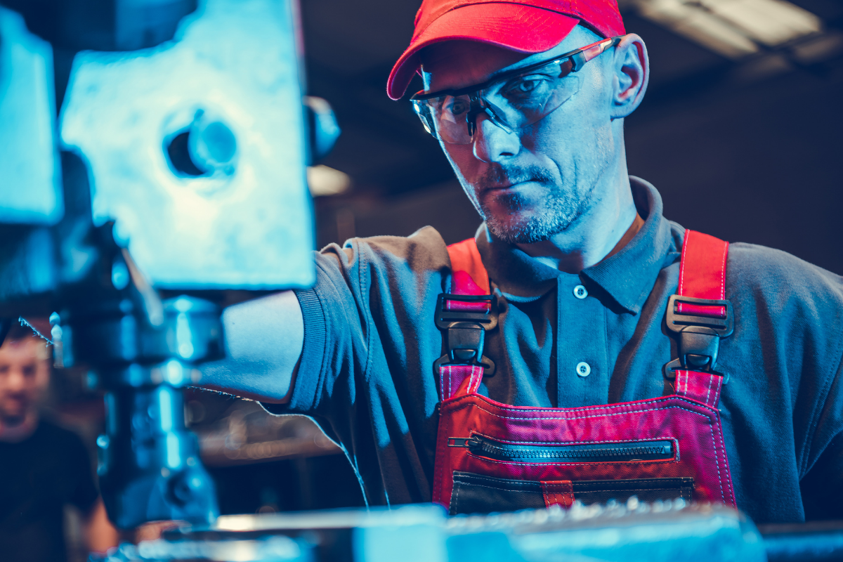 male worker with red hat and safety goggles operates a machine