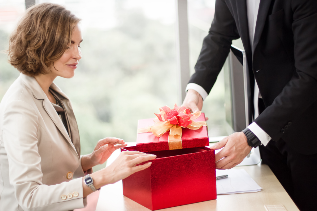 woman at work opens red holiday gift box from coworkers