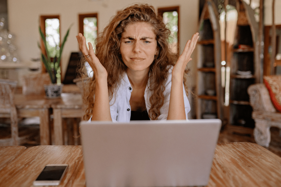 frustrated woman throws her hands up while sitting in front of her laptop