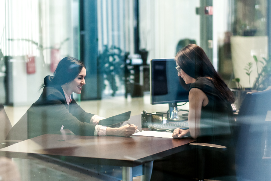 Two female colleagues sit across a desk from each other having an important hiring discussion.