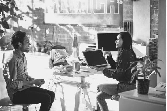 A hiring manager, holding a laptop computer, interviewing a job candidate.