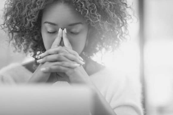 Closeup of stressed-out employee at work, with her eyes closed and hands on face.