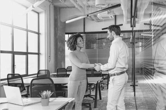 New employee shaking the hand of her new coworker in an office.