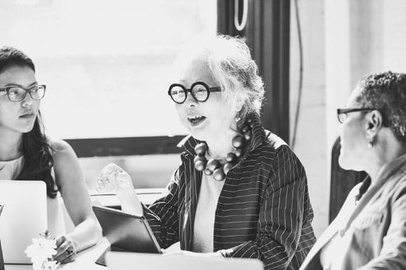 Older woman leading a workplace mentoring programme with two young people.