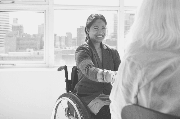 Woman in a wheelchair, shaking hands with a hiring manager, after navigating the stages of the interview process.