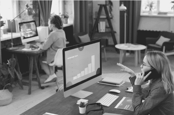 Digital marketing professional working on a campaign (talking on her mobile), with coworker in the background.