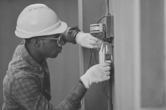 An electrician in a hardhat, installing a component to the wall.