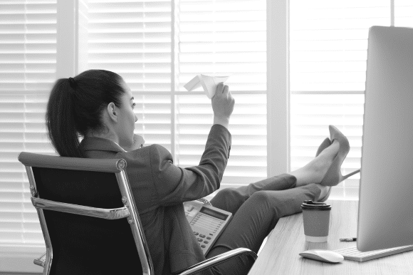 A worker sits with her feet up on the bosses desk, making a personal call and throwing a paper aeroplane, little knowing her boss can see her.