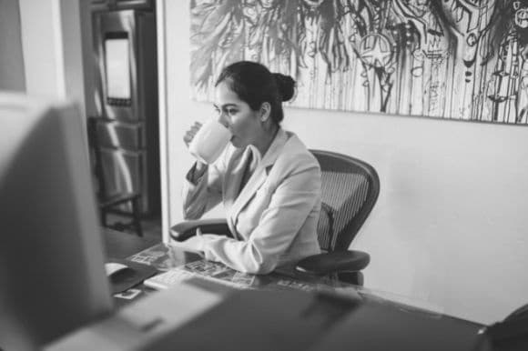 Self-motivated employee, sipping coffee and working at her desk.