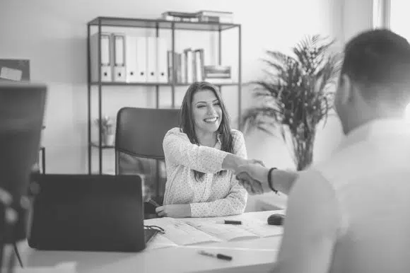 A woman shakes a mans hand over a desk.