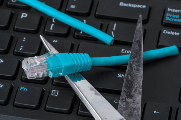 The image shows a pair of scissors cutting through a blue Ethernet cable that is resting on a computer keyboard. This visual metaphor might be used to represent disconnecting from the internet or a symbolic action of cutting off digital communication.