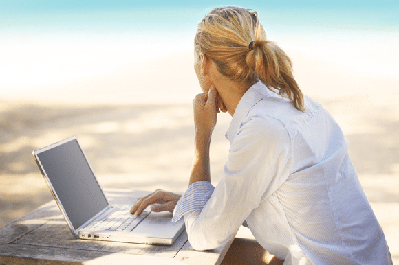 woman at beach on laptop gazing out at the ocean